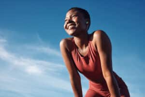 Fitness, Black Woman And Happy Athlete Smile After Running, Exercise And Marathon Training Workout. Blue Sky, Summer Sports And Run Of A African Runner Breathing With Happiness From Sport Outdoor
